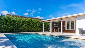 Una piscina con zona de terraza, rodeada por un seto.