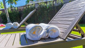 Zona de descanso junto a la piscina con tumbonas de madera y toallas blancas enrolladas.