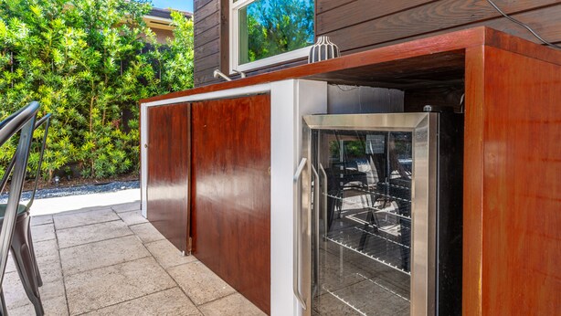 Una cocina con refrigerador de acero inoxidable integrado, armarios de madera y ventana con vistas a un jardín.