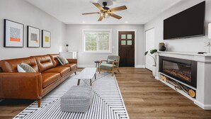 A modern living room with a leather sofa, a coffee table, a fireplace, and a television mounted on the wall. - Modern Bungalow - Endless Recreation, Close to TV (Traverse City)