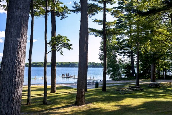 A lakeside park with tall trees, a picnic area, and a dock with people. - Modern bungalow - close to TC with sauna! (Traverse City)