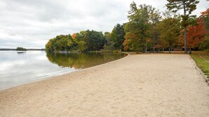 A sandy beach area with a calm lake, surrounded by trees with autumn foliage. - Modern Bungalow - Endless Recreation, Close to TV (Traverse City)