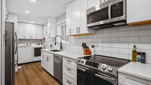 A modern kitchen with white cabinets, stainless steel appliances, and a wooden floor. - Modern Bungalow - Endless Recreation, Close to TV (Traverse City)