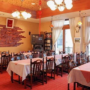 Un área de comedor con varias mesas y sillas, un televisor y una estantería.