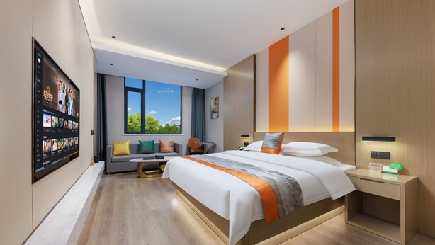 A modern hotel room with a large bed, a desk, a seating area with a sofa and armchairs, a TV mounted on the wall, and a window with a view of greenery. - Ya Chen Hotel (Guangzhou)