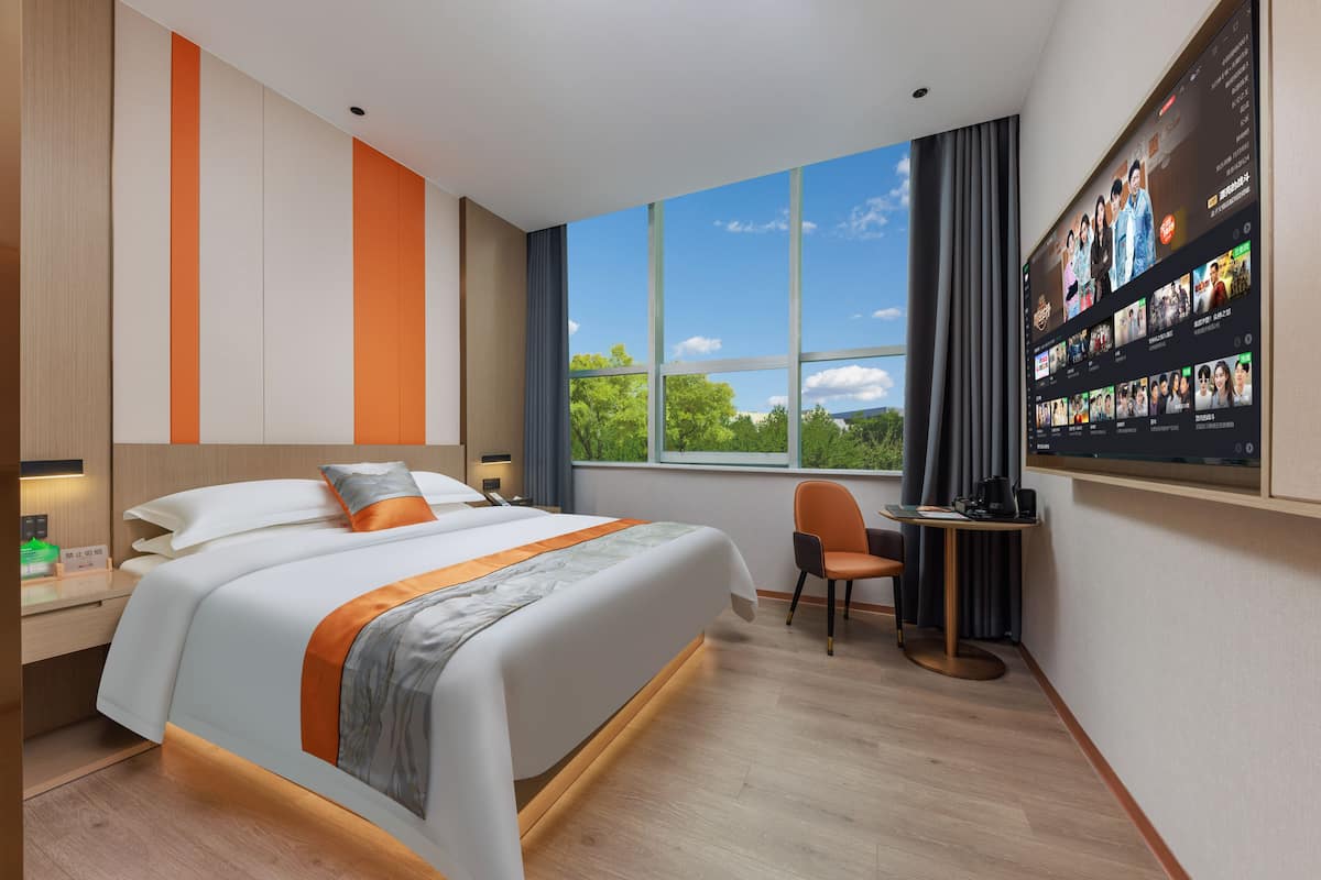 Une chambre d’hôtel moderne avec un grand lit, un téléviseur fixé au mur, une petite table et une chaise.