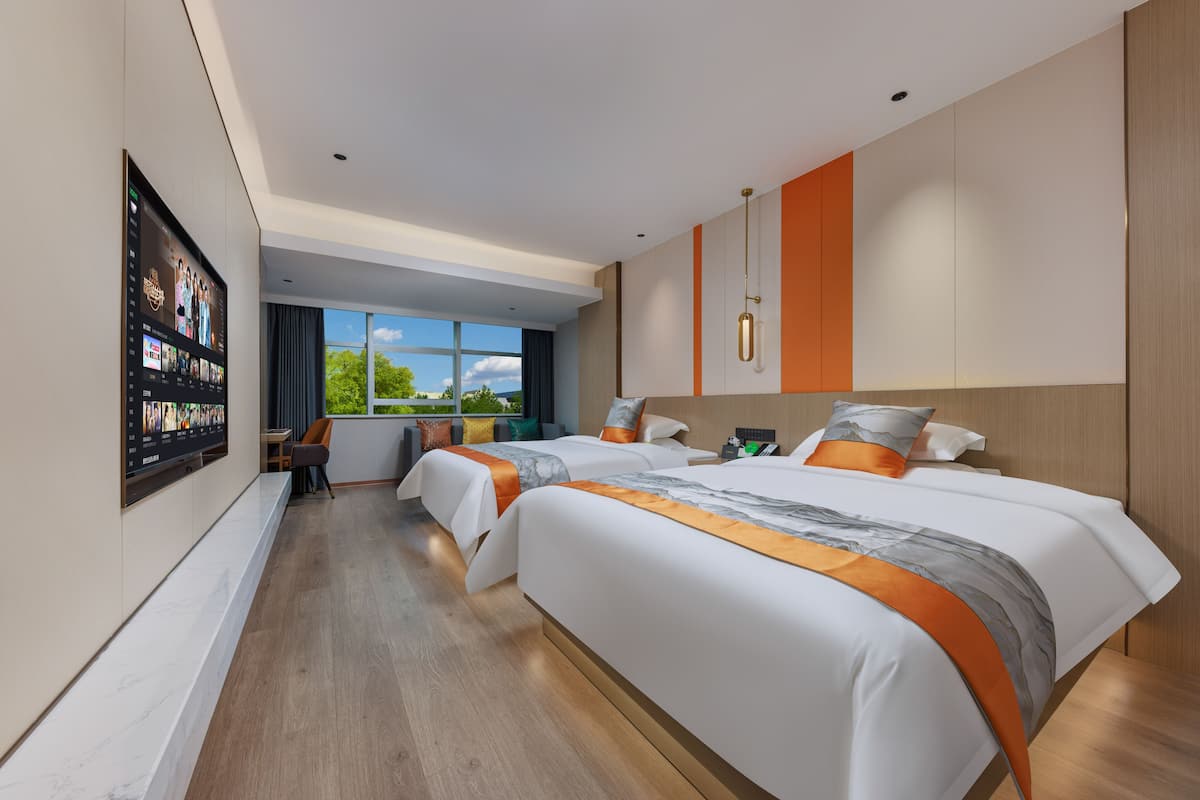 Une chambre d’hôtel moderne, dotée de deux lits, d’une grande fenêtre et d’un téléviseur à écran plat fixé au mur.