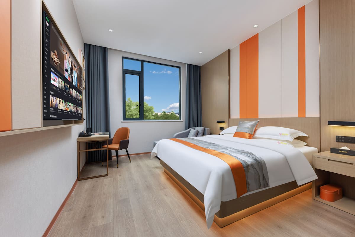 Une chambre d’hôtel moderne, dotée d’un grand lit, d’un bureau et d’un téléviseur fixé au mur.