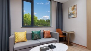 A modern living room with a grey sofa, a round coffee table, and a view of greenery through a large window. - Ya Chen Hotel (Guangzhou)