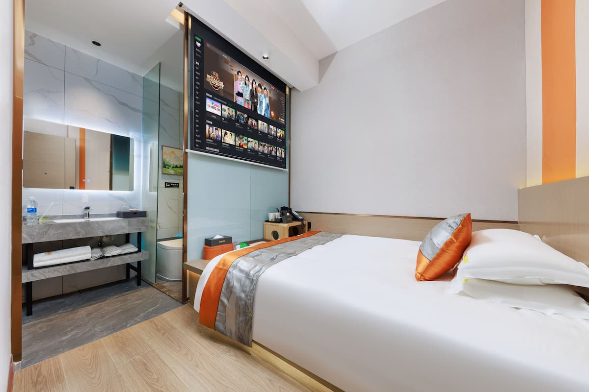 Une chambre d’hôtel moderne dotée d’un grand lit, d’un téléviseur intégré, d’une salle de bain avec un meuble-lavabo et d’un petit coin salon.
