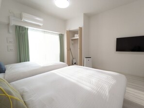 Two single beds with white linens, flat-screen TV, and air conditioning unit.