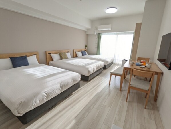 Two single beds with wooden headboards and white bedding, a desk with a chair, flat-screen TV, and a window with an outdoor view.