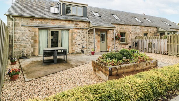 A stone house with a sloped roof, a front door, and a small porch. - Thorneydyke Cottage (Stirling)