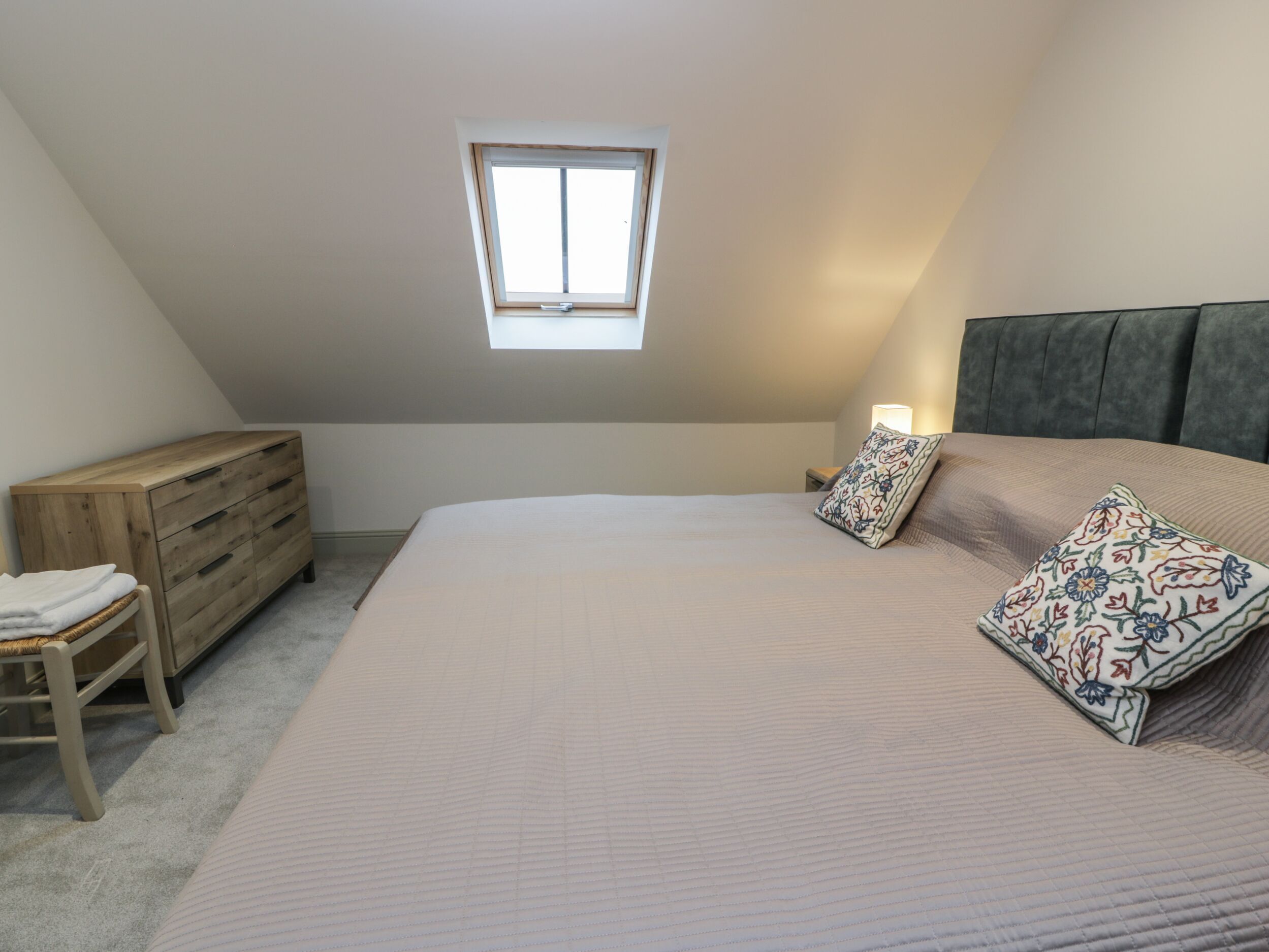 A bedroom with a sloped ceiling, a bed with a floral pillow, a wooden dresser, and a small window.