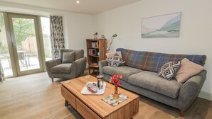 A living room with a sofa, armchair, wooden coffee table, bookshelf, and a painting on the wall. - Thorneydyke Cottage (Stirling)