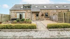 A stone house with a tiled roof, a front door, and a small garden with hedges and flower beds. - Thorneydyke Cottage (Stirling)