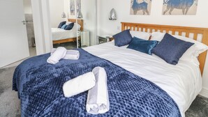 Hotellihuone, jossa on sänky, peili, yöpöytä ja taideteos seinällä.