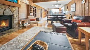 A cozy living room with a stone fireplace, leather sofas, a dining area, and wooden walls.