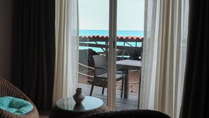 A room with a view of the beach through a large window. There is a wicker chair with a teal cushion and a small round table with a vase. - La Palma Beachfront Hotel Boutique (Cancun)