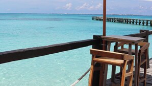 A wooden deck with a table and chairs overlooking turquoise waters and a pier in the distance. - La Palma Beachfront Hotel Boutique (Cancun)