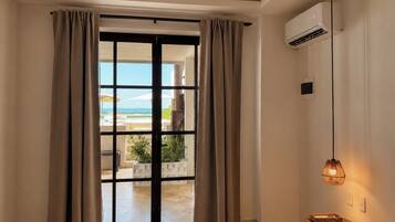 Una camera d'albergo con una porta-finestra scorrevole che dà su un balcone, un letto, un comodino, un condizionatore e un lampadario.
