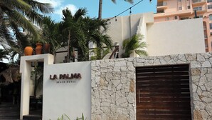 The exterior of La Palma Beach Hotel with a stone facade, a large wooden gate, and palm trees. - La Palma Beachfront Hotel Boutique (Cancun)