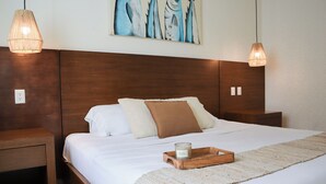 A neatly made bed with white linens, a brown throw pillow, and a wooden tray with a candle. There is a painting of fish on the wall above the bed. - La Palma Beachfront Hotel Boutique (Cancun)