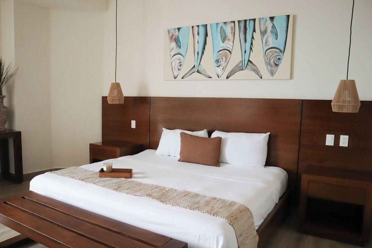 Quarto bem organizado com uma cama grande, cabeceira de madeira, mesas de cabeceira e uma obra de arte pendurada na parede.