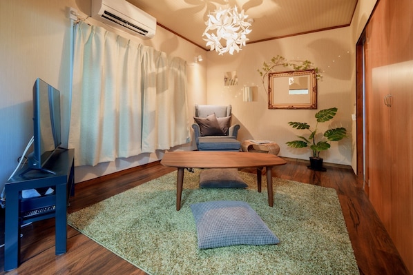 A room with a wooden coffee table, a blue armchair, a TV on a stand, a potted plant, and a mirror on the wall.