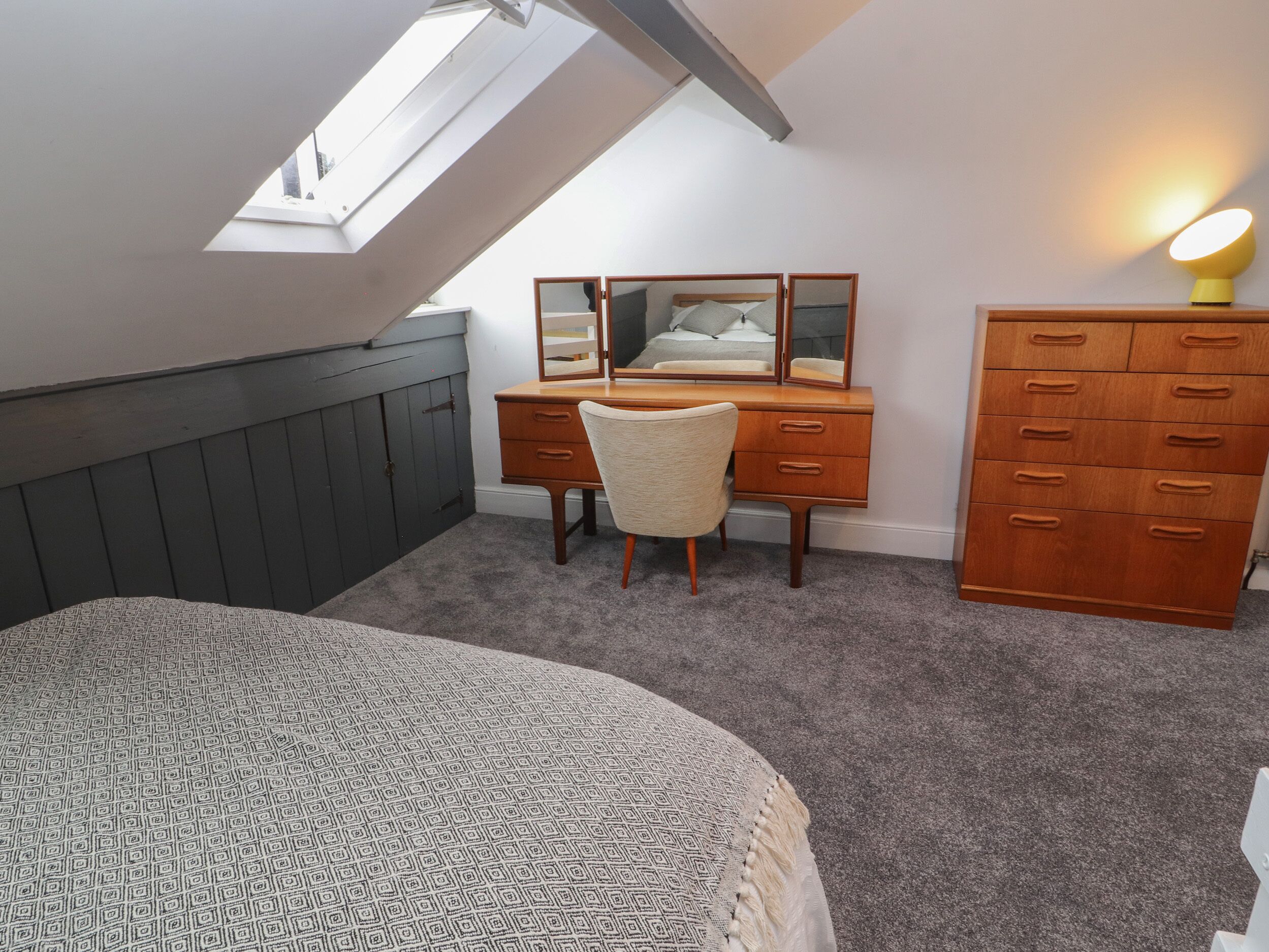A bedroom with a sloped ceiling, a bed, a desk with a chair, a dresser, and a mirror.