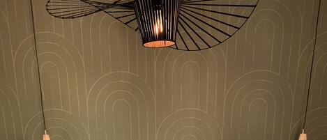 A neatly made bed with a floral pillow, two bedside tables, and a modern pendant light fixture.