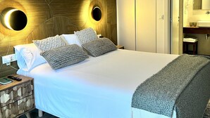 A modern bedroom with a large bed, a wooden headboard, two wall sconces, a bedside table, and a nightstand. - La Costera Hostal del Vino (Altea)