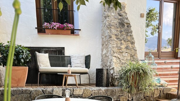 An outdoor patio with a round table and chairs, a stone wall, and potted plants. - La Costera Hostal del Vino (Altea)