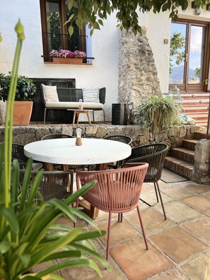 Un patio al aire libre con una mesa redonda y sillas, un muro de piedra y plantas en macetas.