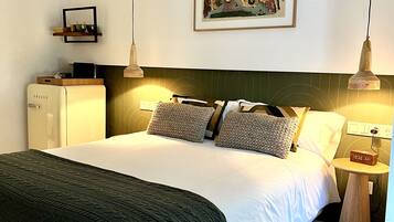 A neatly arranged hotel room with a bed, bedside lamps, a small table, a clock, and a painting on the wall.