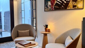 A modern interior with a round wooden table, two armchairs, a large abstract painting, and a view of the outside through a window. - La Costera Hostal del Vino (Altea)