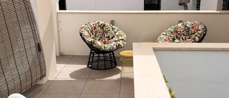 A rooftop terrace with two floral-patterned chairs, a small round table, and a swimming pool.