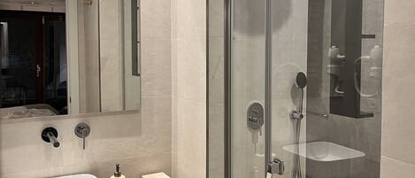 Un baño moderno con ducha envuelta en vidrio, un lavamanos blanco y un mueble de tocador de madera.