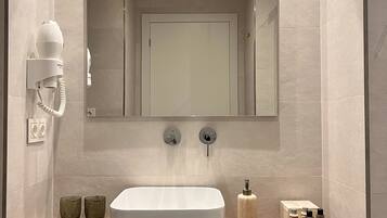 Een moderne badkamer met een grote spiegel, een houten wastafelmeubel, een witte wasbak en een föhn bevestigd aan de muur.