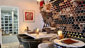A wine cellar with a wall of wine bottles, a dining area with tables and chairs, and a wine rack with bottles. - La Costera Hostal del Vino (Altea)