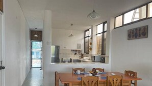 A dining area with a wooden table and chairs, a kitchen in the background, and large windows. - Casa de Playa Cahuve Frente al mar (Cardalito)