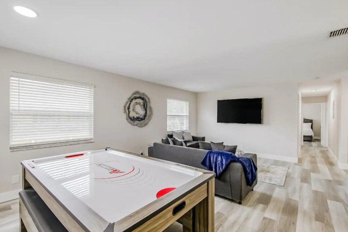 A modern living room with a pool table, a grey sofa, and a flat-screen TV on the wall.