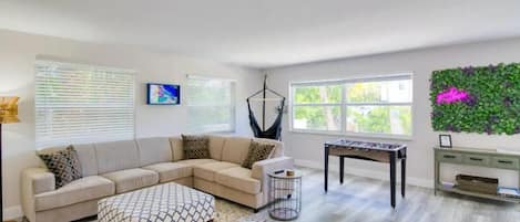 A living room with a sectional sofa, a coffee table, a foosball table, and a wall-mounted plant.