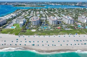 Un complejo turístico costero con varios edificios de gran altura, una playa arenosa con numerosas sombrillas y vistas al océano y al perfil distante de la ciudad.
