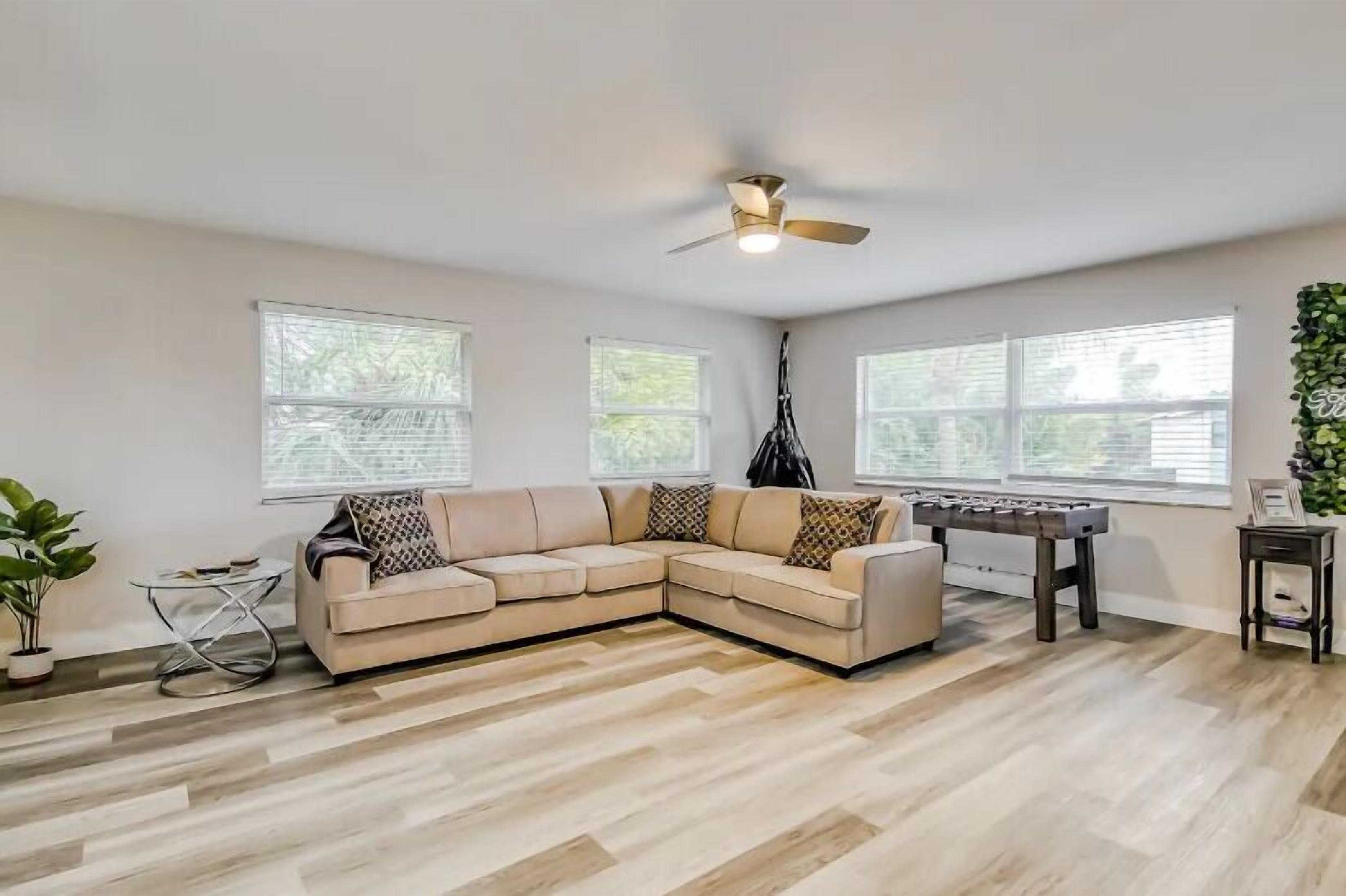 A living room with a sectional sofa, a ceiling fan, and a foosball table.