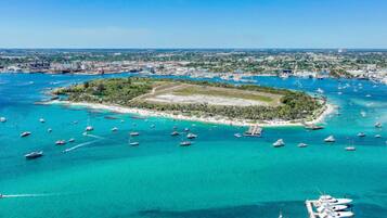 An aerial view of a tropical island with clear turquoise waters, surrounded by a marina with numerous boats.