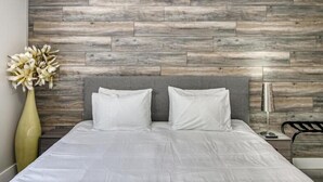 A modern bedroom with a grey headboard, white bedding, and a wooden wall panel. - Isla Palma Singer Island (Singer Island)