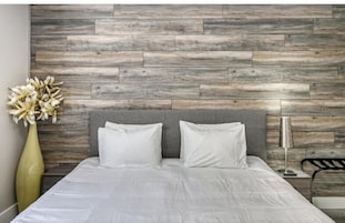 Un dormitorio moderno con cabecera gris, ropa de cama blanca y un panel de pared de madera.