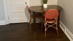 Un coin repas avec une table ronde, deux chaises en osier, une plante en pot et un tableau encadré au mur.