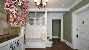 Un escalier avec une rampe blanche menant à un palier, une porte blanche avec une plaque numérotée et un lustre au-dessus.